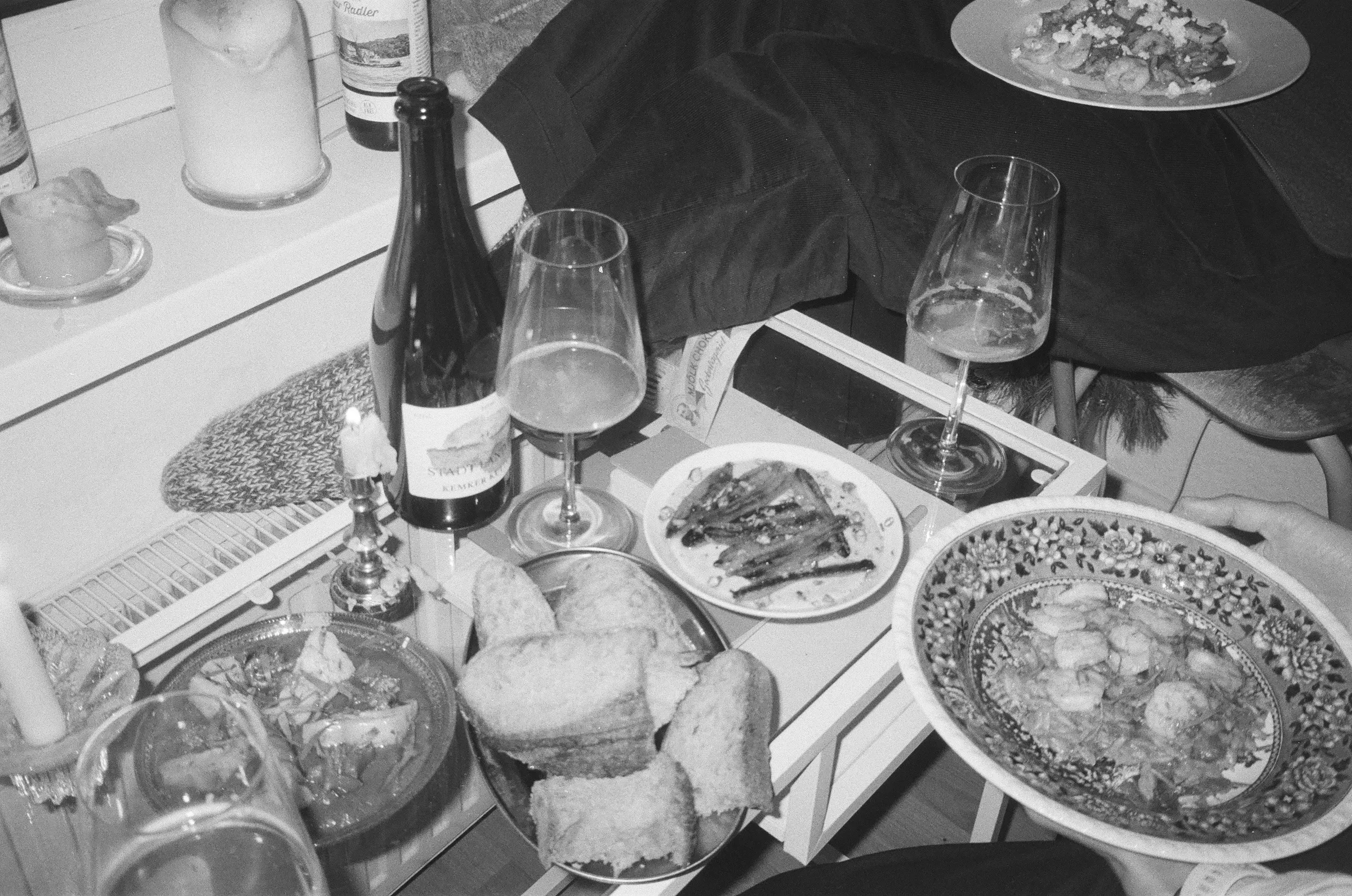 Mesa compartida en blanco y negro con una botella de vino, copas, pan y velas